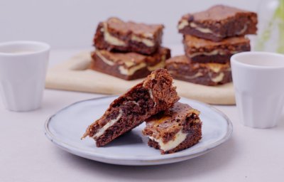 De browniecheesecake ligt op een bordje aangesneden. Dit is eigenlijk een brownie in combinatie met cheesecake, zo verkrijg je een marmereffect in je brownie door het mengsel met de roomkaas. 